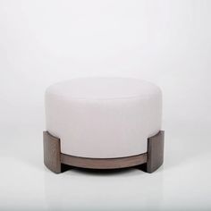 a white ottoman sitting on top of a wooden stand in front of a white wall