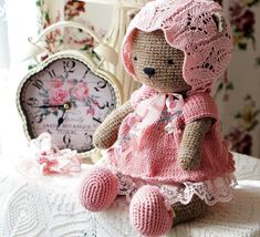 a crocheted teddy bear sitting on top of a table next to a clock