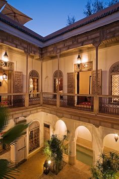 an outdoor courtyard at night with potted plants and lights on the balconies