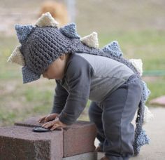 a small child wearing a crocheted hat and playing with a cell phone outside