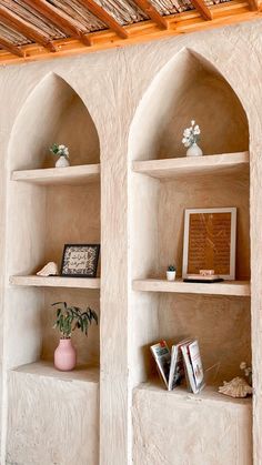 two stone shelves with vases and books on them in a room that has wood beams