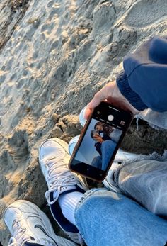 a person sitting in the sand with their cell phone