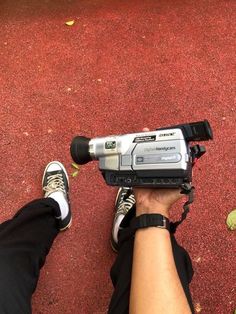 a person is holding a video camera in their right hand while sitting on the ground