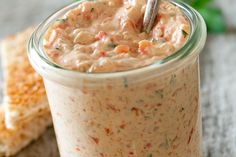 a glass jar filled with food sitting on top of a table next to crackers