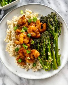 a white plate topped with rice and broccoli covered in sauce next to a bowl of vegetables