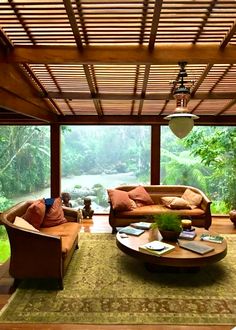 a living room filled with lots of furniture and large glass doors leading to a lush green forest