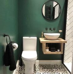 a white toilet sitting next to a sink in a bathroom under a round mirror on a wall