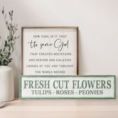 a wooden sign sitting on top of a table next to a vase with flowers in it