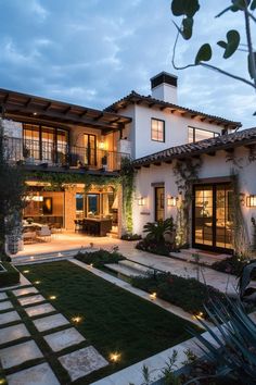 a large white house with lots of windows and plants in the front yard at dusk