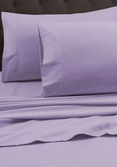 a bed with purple sheets and pillows on it