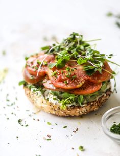 a bagel with tomatoes, lettuce and herbs on it