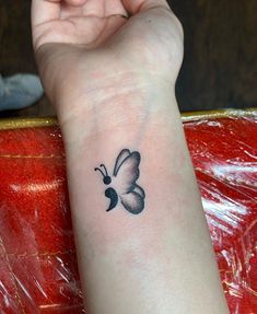 a small butterfly tattoo on the left wrist and right hand is shown in black ink