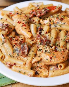 a white plate topped with pasta covered in sauce and chicken breast pieces, garnished with parsley