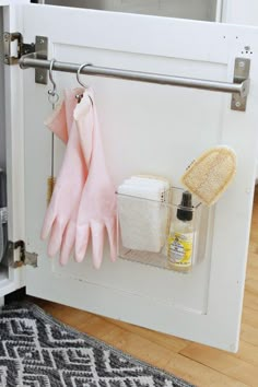 a pair of pink gloves hanging on a door handle next to cleaning supplies and sponges