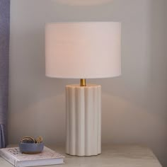 a white lamp sitting on top of a table next to a book