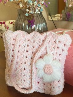 a pink crocheted purse sitting on top of a table next to a vase with flowers