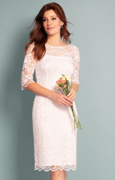 a woman in a white dress holding a bouquet of flowers and posing for the camera