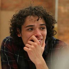 a young man with curly hair sitting at a table looking to his left and smiling