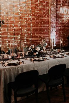 a table set up with place settings and flowers in front of a brick wall that says now on it