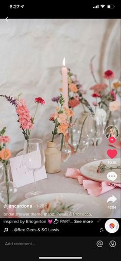 the table is set with pink and orange flowers in vases, candles, and cards