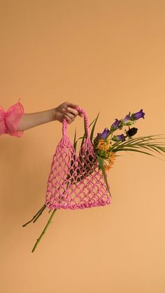 a person is holding a pink bag with flowers in it and the handles are made out of woven material