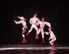 four men in white and red outfits are performing on stage with one man jumping up into the air