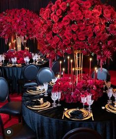 the table is set with black linens and gold place settings, surrounded by red roses