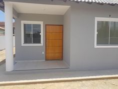 a grey house with a wooden door and window on the front porch, in an empty lot