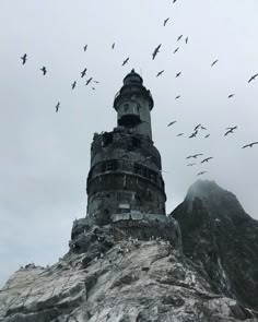 birds flying around a tower on top of a mountain