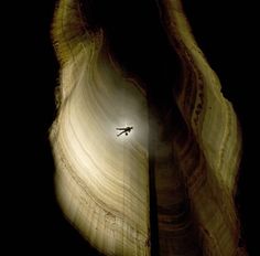 an airplane is flying through the dark sky above some rocks and water, with light coming from behind it