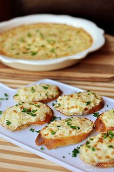 several pieces of bread with cheese and parsley on them sitting on a plate next to a casserole dish