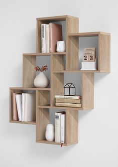 a wooden shelf filled with books on top of a white wall next to a vase