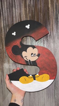 a hand holding up a wooden letter with a mickey mouse face painted on the front