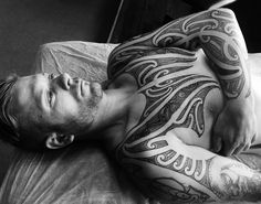 a man laying on top of a bed with lots of tattoos on his chest and arms