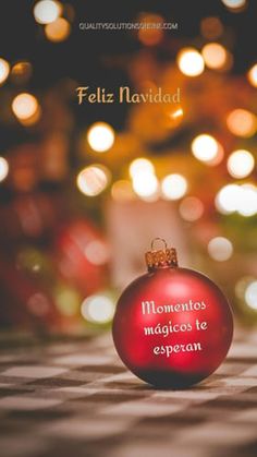 a red ornament sitting on top of a table next to christmas lights with the words feliz naviddad