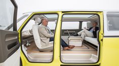 two men sitting in the driver's seat of a small yellow vehicle with its doors open