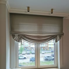 a window with an open roman blind in front of it and cars parked on the street outside