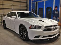 a white dodge charger parked in a garage next to a man and his dog