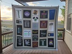 a large quilt hanging on the side of a wooden porch next to a fence and trees