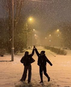 two people are standing in the snow holding their hands up to each other while they stand under street lights