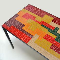 a multicolored table with black metal legs and a white surface that has squares on it