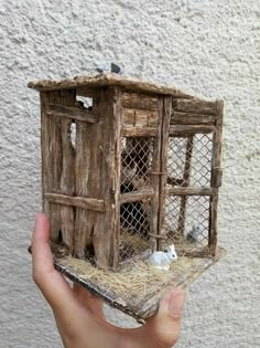 a hand holding a small wooden birdhouse with sheep inside it and hay in the roof