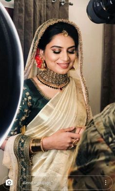 a woman in a white and green sari smiles as she looks at her cell phone