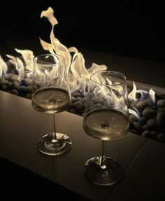 two wine glasses sitting next to each other on top of a table with fire in the background