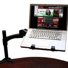 an open laptop computer sitting on top of a wooden desk next to a black arm