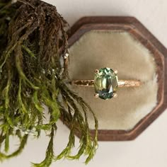 a ring sitting on top of moss next to a piece of wood with a green stone in it