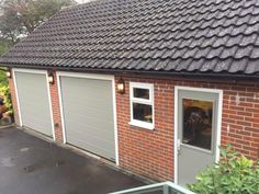 a garage with two doors and windows on the outside, in front of a brick building