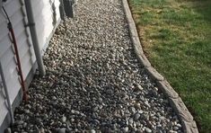 a gravel path next to a house with grass and bushes on the side of it