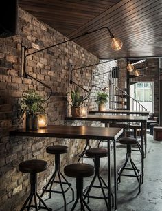 a brick wall with several stools and tables in front of it, along with lights hanging from the ceiling