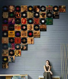 a woman sitting on top of a wooden bench next to a wall covered in records